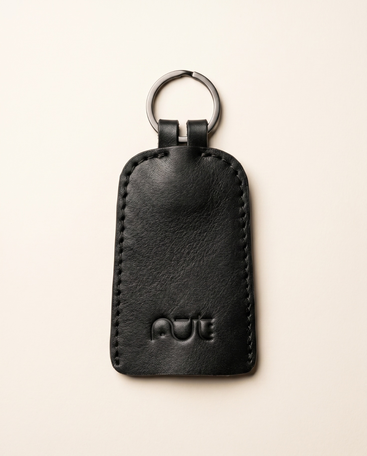 Black leather keychain with stitched edges and embossed nūt logo.